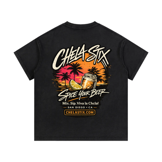 A black short-sleeve t-shirt with a large graphic on the back. The graphic features the text 'CHELA SIX' in a stylized white font, a sunset illustration with palm trees, a beer can, and a lime wedge, with the phrase 'SPICE YOUR BEER' and 'SAN DIEGO * CA' below.