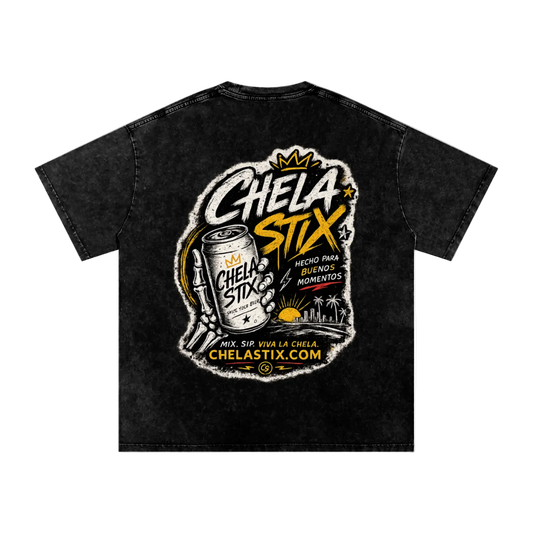 A black acid-wash t-shirt featuring a large back graphic for 'Chela Stix'. The graphic includes a hand holding a can of Chela Stix, a crown, and the text 'Chela Stix' in stylized white and yellow lettering, along with 'Hecho para enfrentar momentos' and 'ChelaStix.